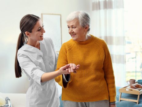 Pflegekraft stützt eine ältere Frau beim Gehen